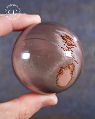 A hand holding a Peach Moonstone sphere from Madagascar