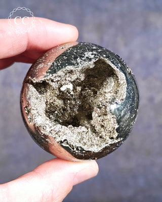 A hand holding a polished Pyrite Sphere from Peru with crystallised cavities