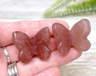 A hand holding two Raspberry Aventurine Butterfly carvings 