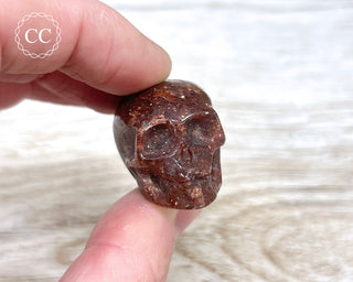 Fingers holding a red Aventurine crystal skull carving
 