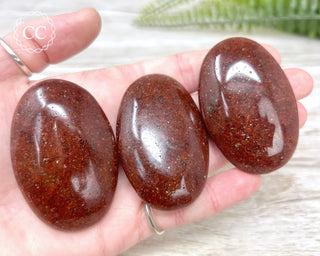 A hand holding three Red Aventurine crystal palmstones