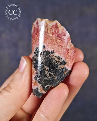 A hand holding a Rhodochrosite part polished freeform from Argentina