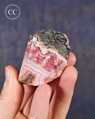 A hand holding a Rhodochrosite part polished freeform from Argentina