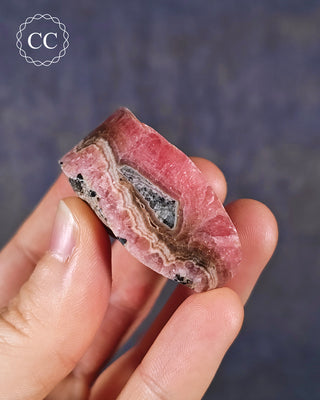 A hand holding a Rhodochrosite part polished freeform from Argentina