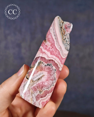 A hand holding a Rhodochrosite part polished freeform from Argentina