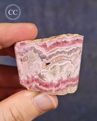 A hand holding a Rhodochrosite part polished freeform from Argentina