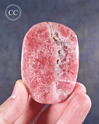 A hand holding a Rhodochrosite freeform from Argentina 