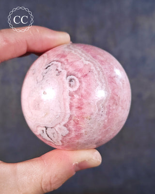 A hand holding a Rhodochrosite sphere from Peru