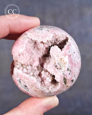 A hand holding a Rhodochrosite sphere from Peru with crystalline pockets
