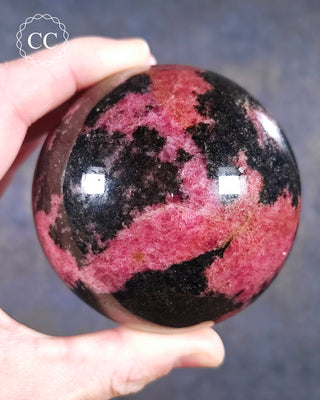 A hand holding a Rhodonite sphere from Madagascar