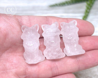 A hand holding 3 Rose Quartz Fox Carvings