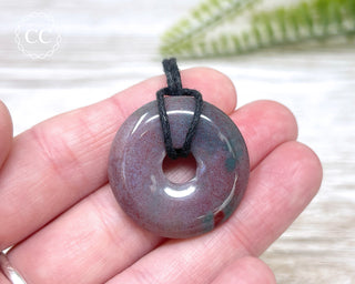A hand holding a Sea Jasper donut pendant on a black cord 