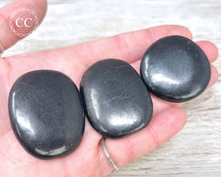 A hand holding three Shungite Palmstones