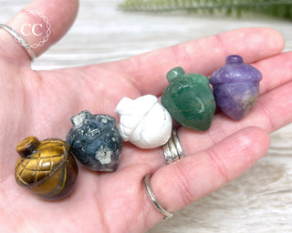 A hand holding 5 small crystal acorn carvings in various crystal type