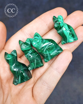 Malachite cat carvings on hand on blue background