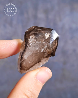 A hand holding an Smoky Elestial Quartz is from Brazil