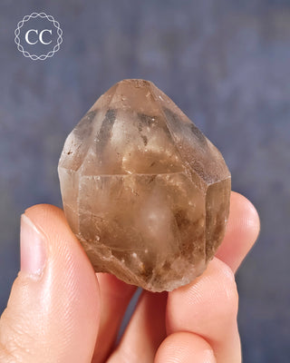 A hand holding a natural Smoky Quartz crystal from Brazil