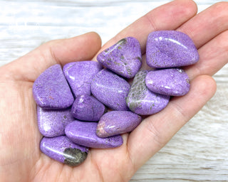 A hand holding a selection of Stichtite tumbled crystals 