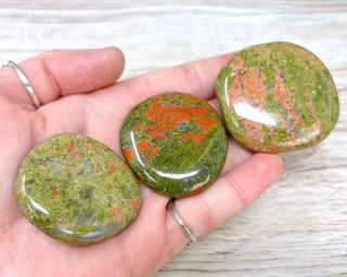 A hand holding three Unakite Palmstones