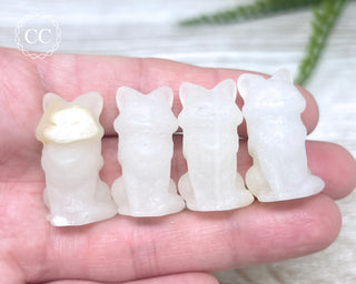 A hand holding 4 White Calcite Fox carvings